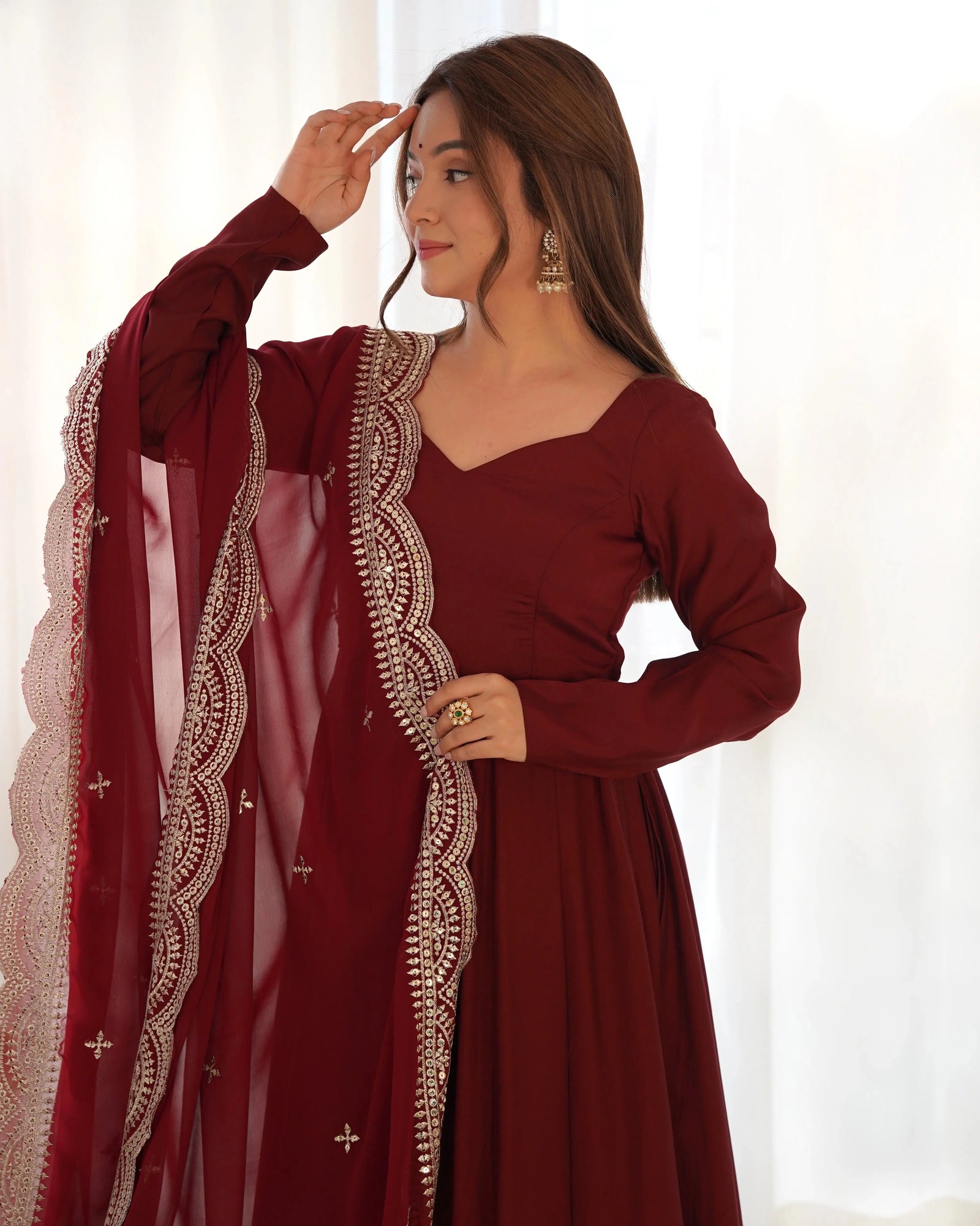 Woman wearing a maroon traditional outfit with intricate designs on a white background