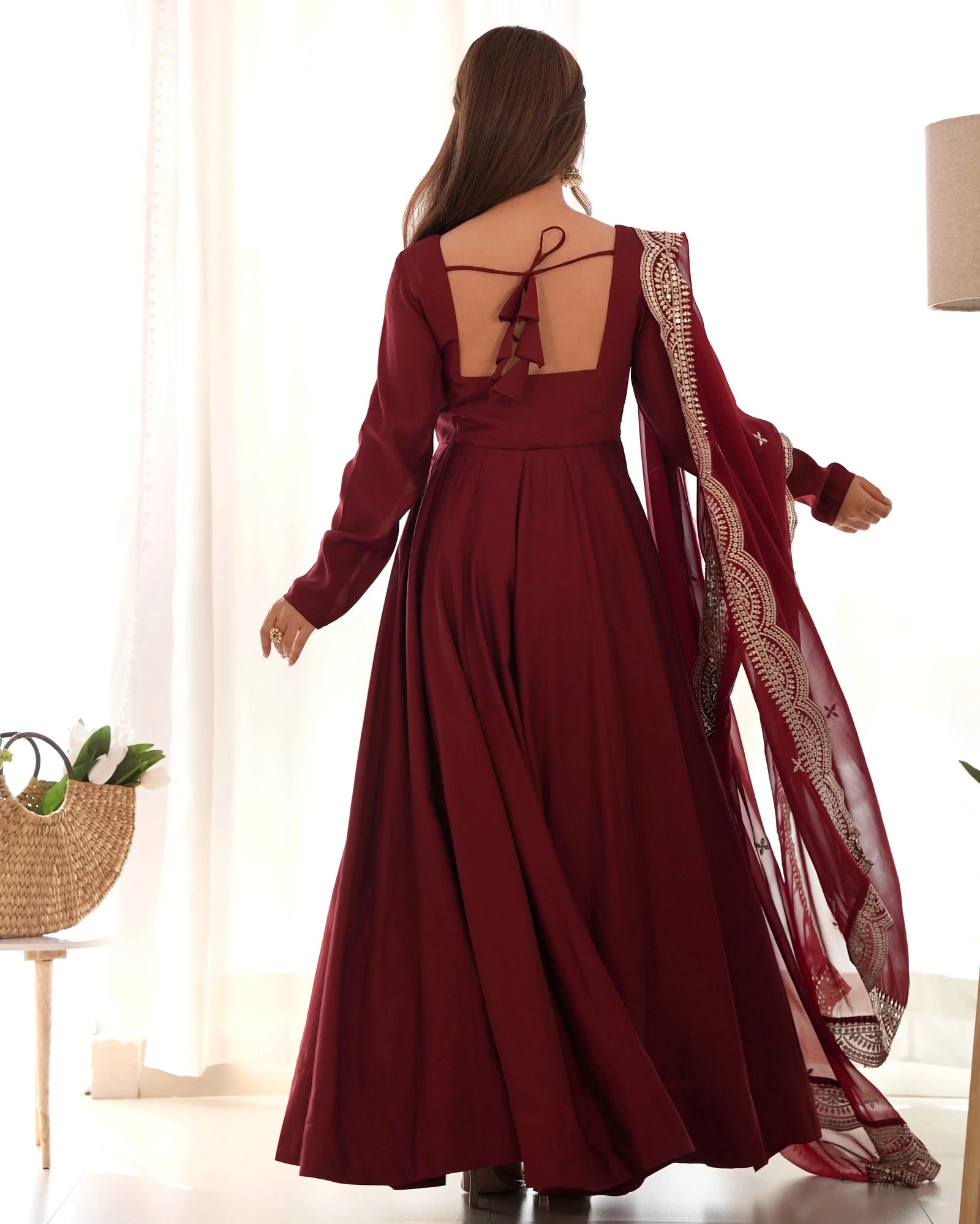 Woman wearing a burgundy dress with intricate sleeves in a bright room.