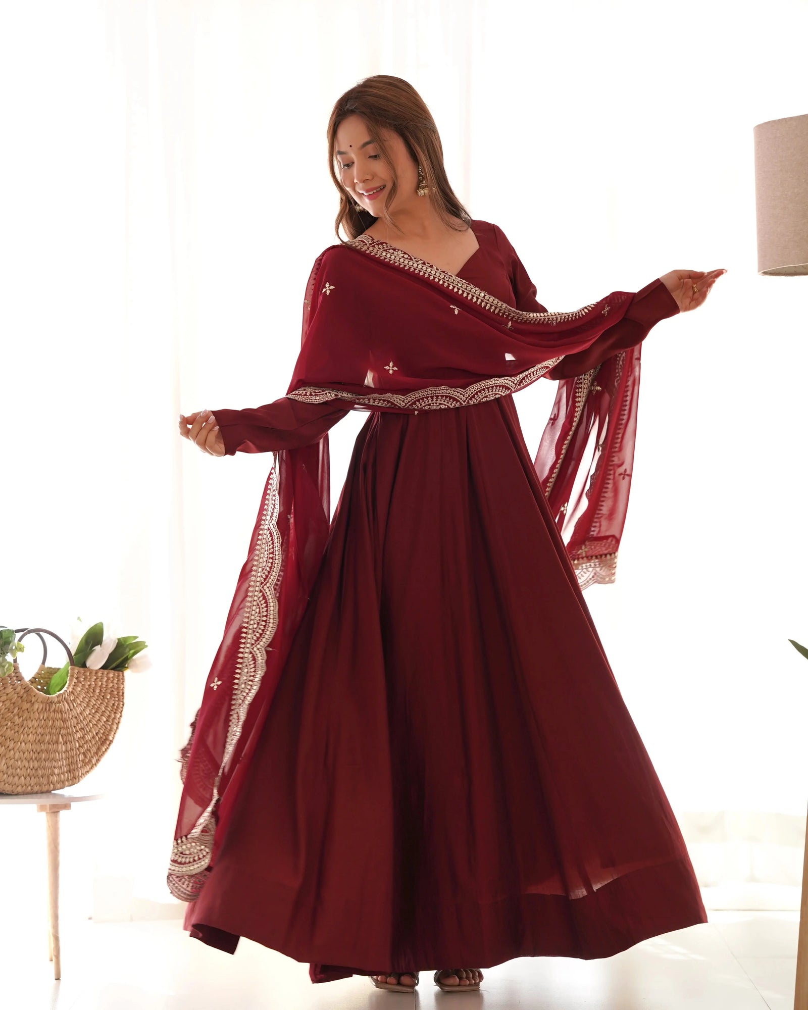 Woman wearing a burgundy dress with gold embroidery in a bright room.