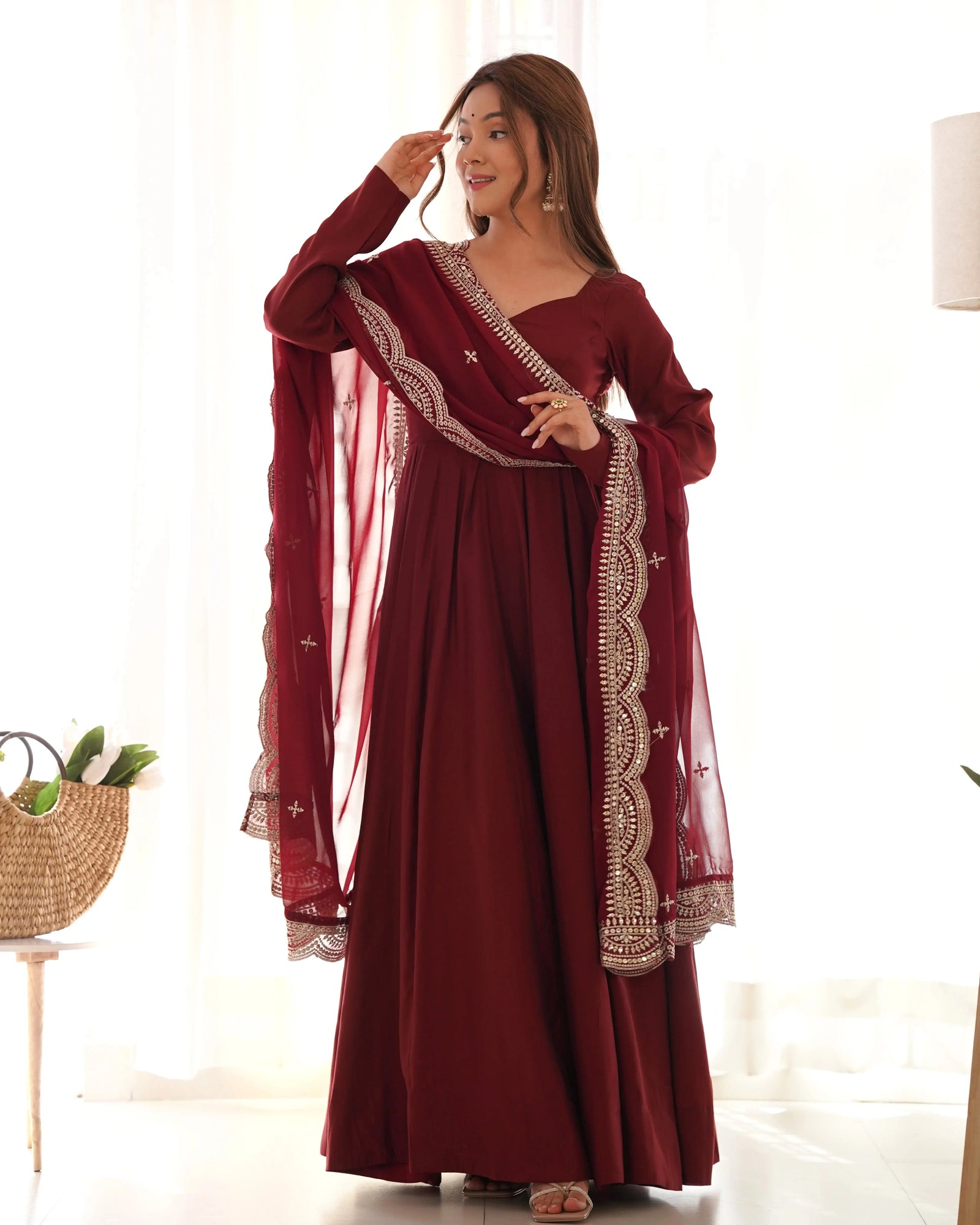 Woman wearing a burgundy dress with white embroidery in a bright room.
