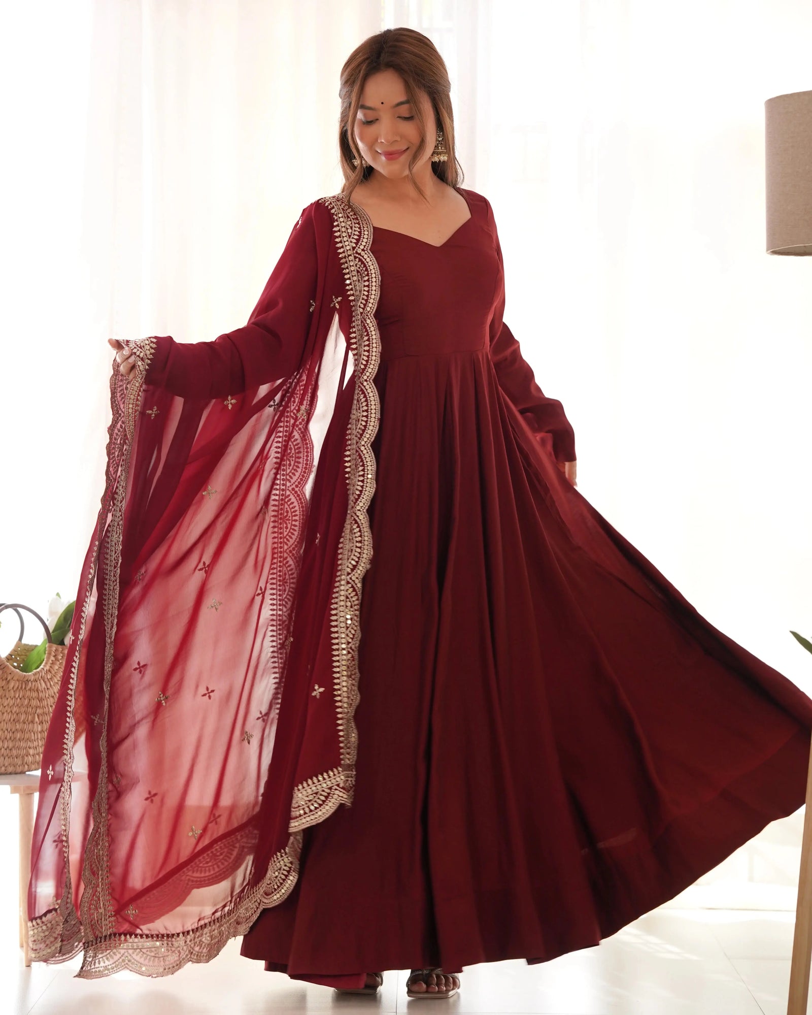 Woman wearing a burgundy dress with lace details in a bright room.