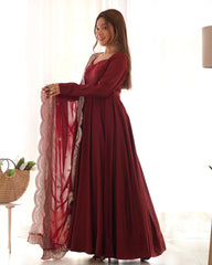 Woman wearing a long burgundy dress with a sheer red overlay in a bright room.