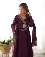Woman wearing a purple dress with intricate designs in a bright room.