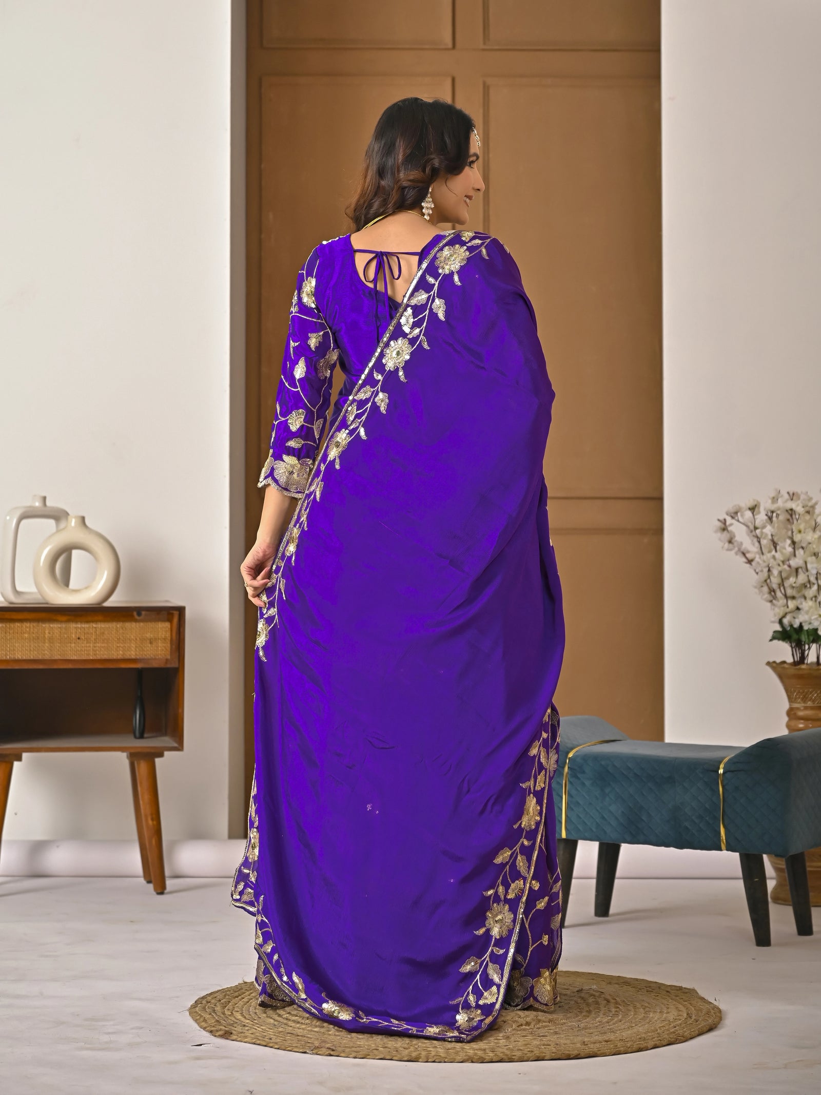 Woman wearing a purple saree with gold embroidery in a room setting.