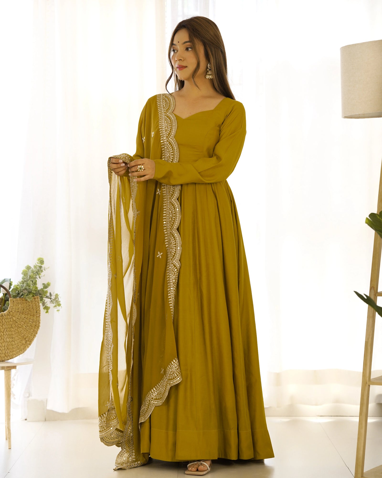 Woman wearing a mustard yellow dress with lace details in a bright room.