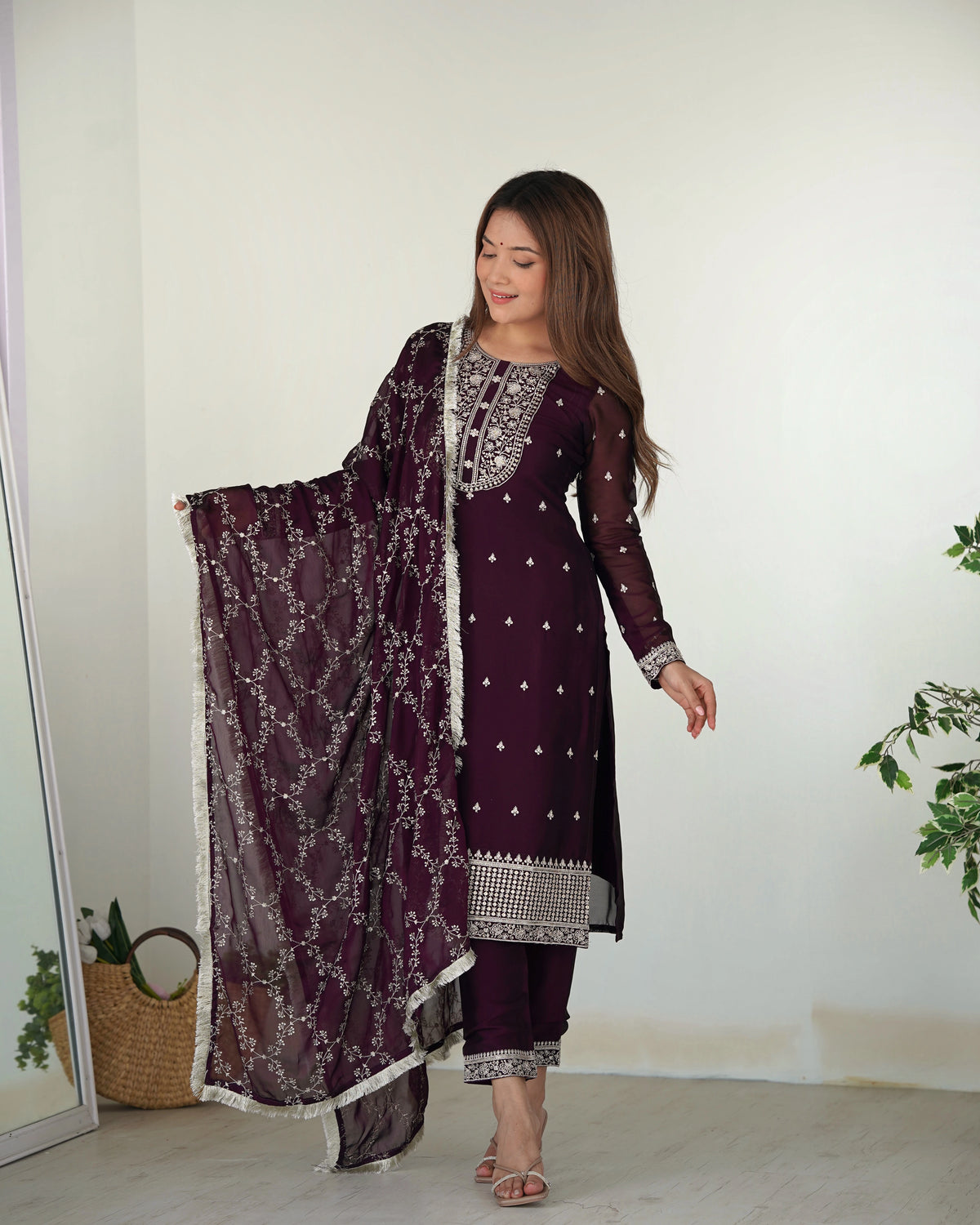 Woman wearing a purple traditional outfit with a matching dupatta in a minimal indoor setting.