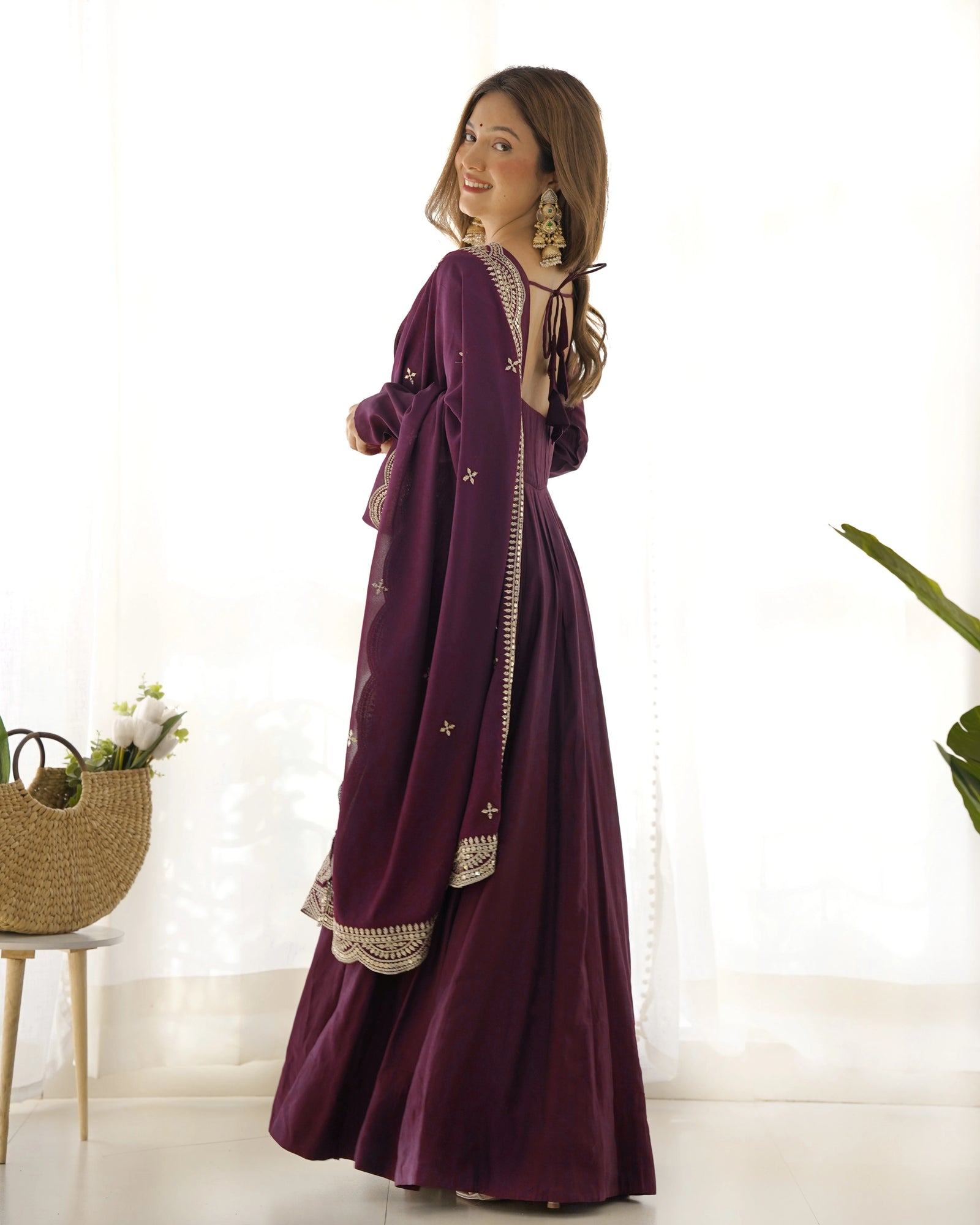 Woman wearing a long, dark purple dress with intricate patterns in a bright room.