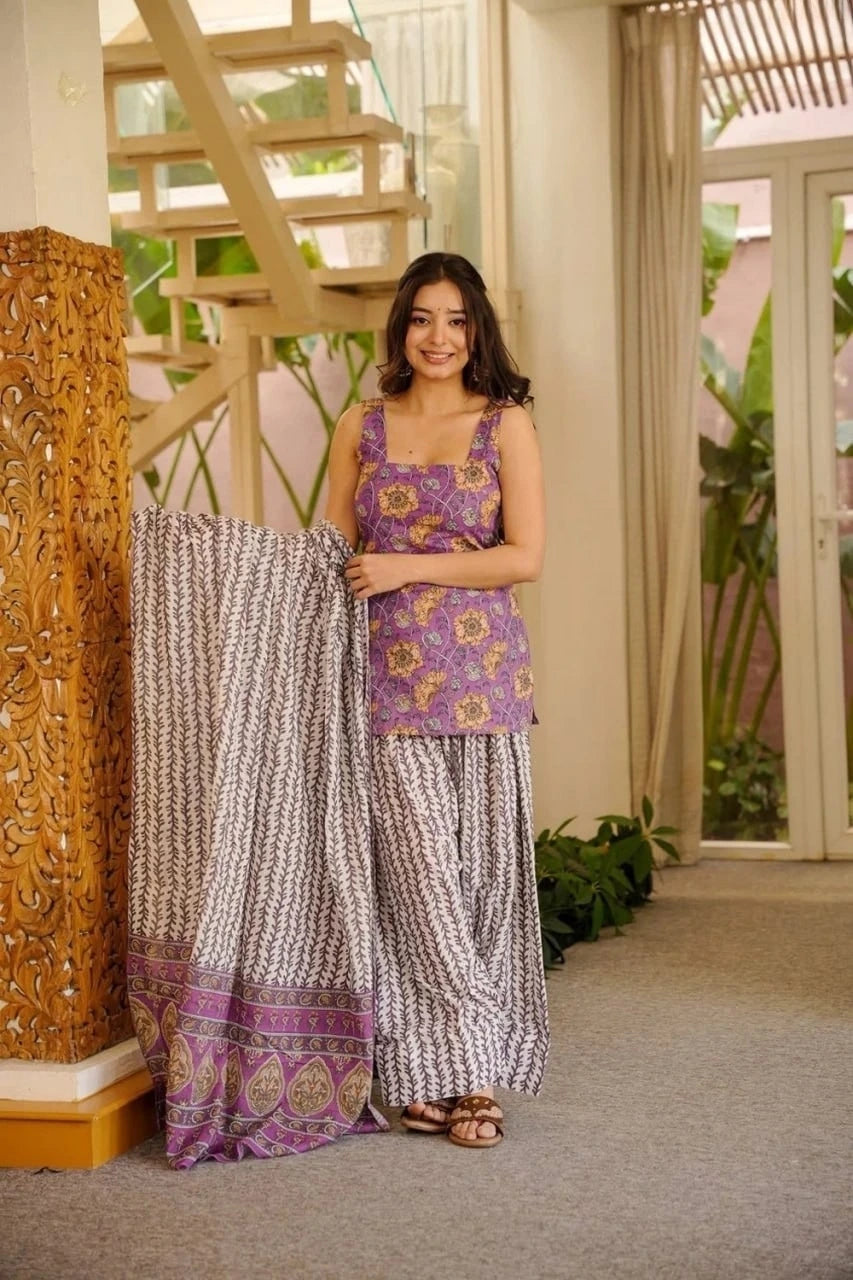 Woman in a purple top and patterned skirt standing indoors with decorative elements.