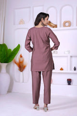 Woman wearing a mauve outfit standing in a minimalistic room with white shelves and decorative items.