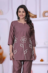 Woman wearing a mauve outfit with floral embroidery against a white background