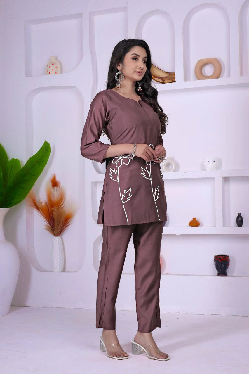 Woman wearing a brown outfit with white embroidery in a minimalistic room.
