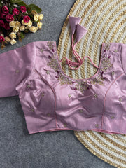 The front of the lavender silk blouse shows a curved V-neckline with matching pearl and gold floral embroidery. The bodice is structured with princess-cut seams and adorned with scattered pearl floral motifs. The blouse is laid flat on a grey textured surface next to a decorative jute mat and a bouquet of roses.
