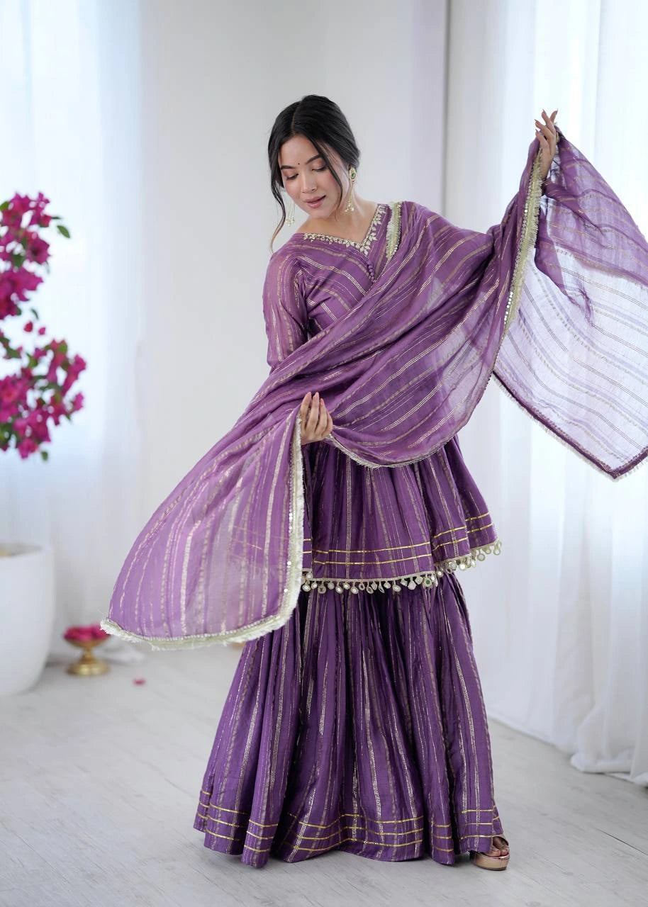 Woman wearing a traditional purple outfit with a matching dupatta in a bright room.