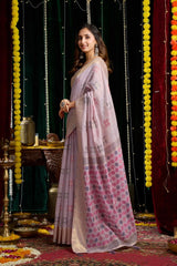 Woman in a pink saree with floral patterns standing in a decorated indoor setting.