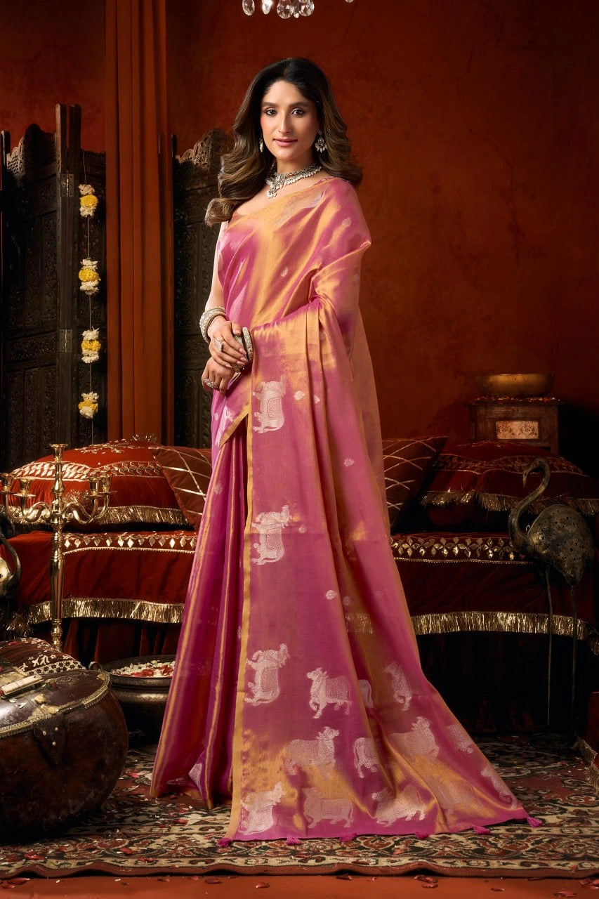 Woman in a pink saree with a patterned design standing in an ornate room.