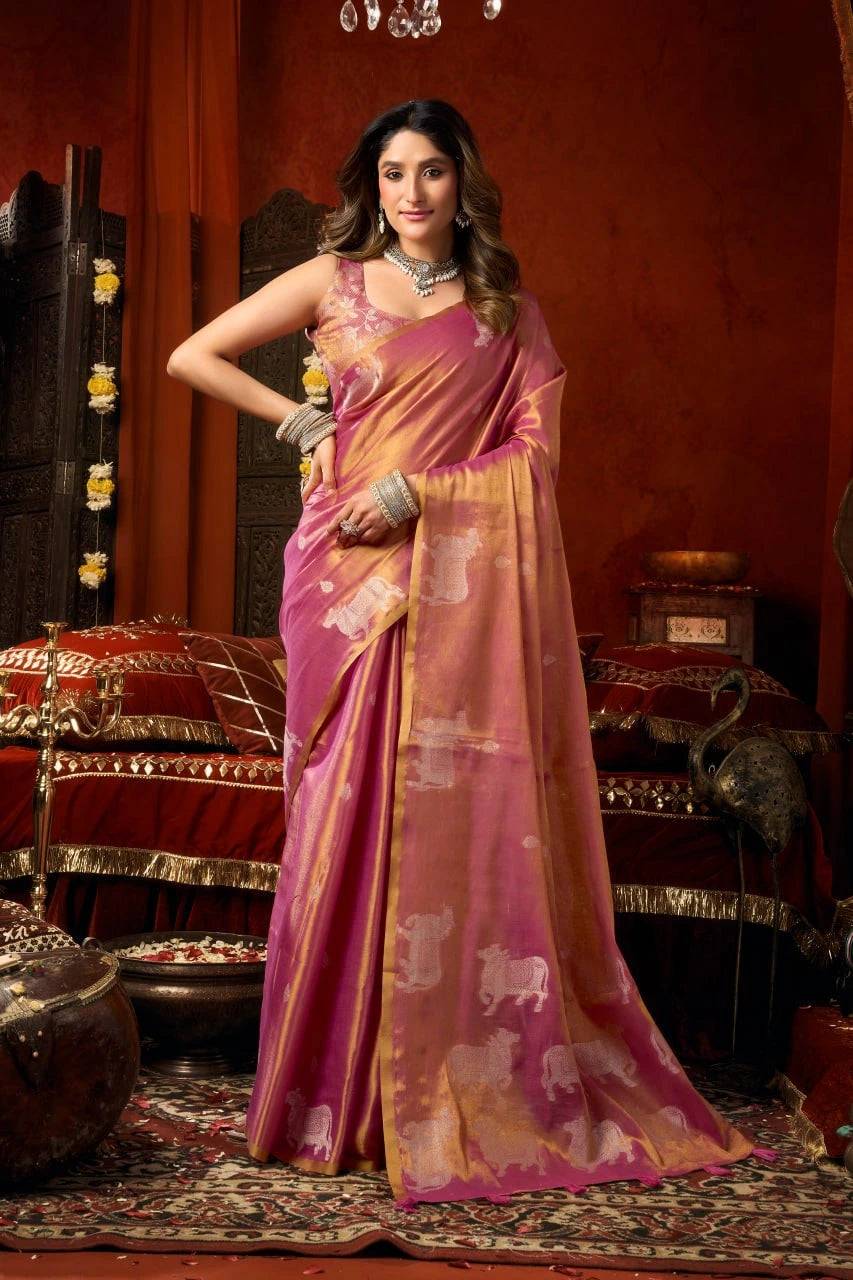 Woman in a pink and gold saree standing in an ornate room.