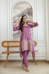 Woman in a purple traditional outfit sitting on a wooden bench with a decorative wall in the background