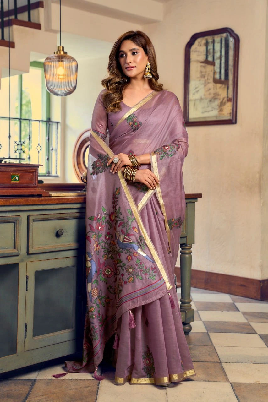 Woman in a purple saree with floral patterns standing in a room with a mirror and cabinet.