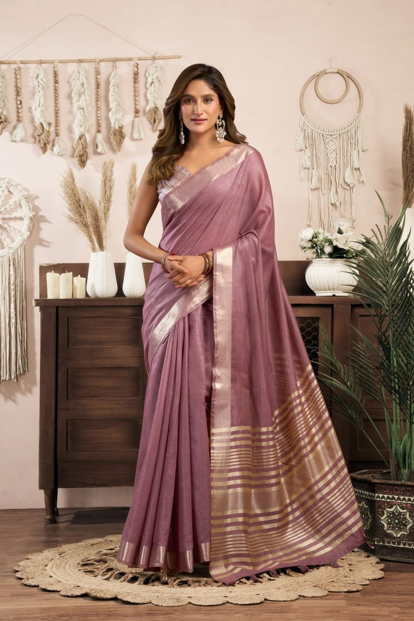 Woman in a mauve saree with a white blouse standing in a decorated room.