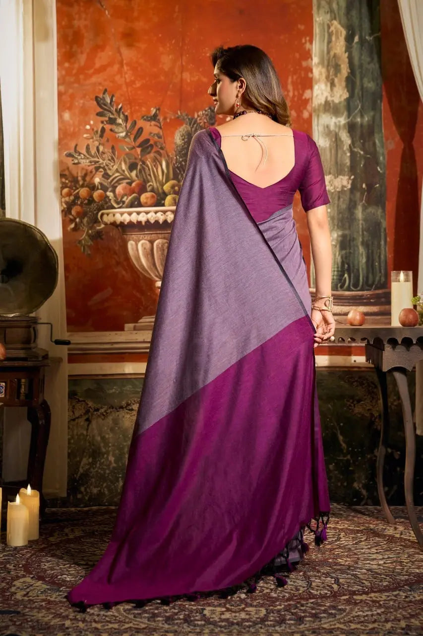 Woman wearing a purple and gray saree in an indoor setting with decorative elements.