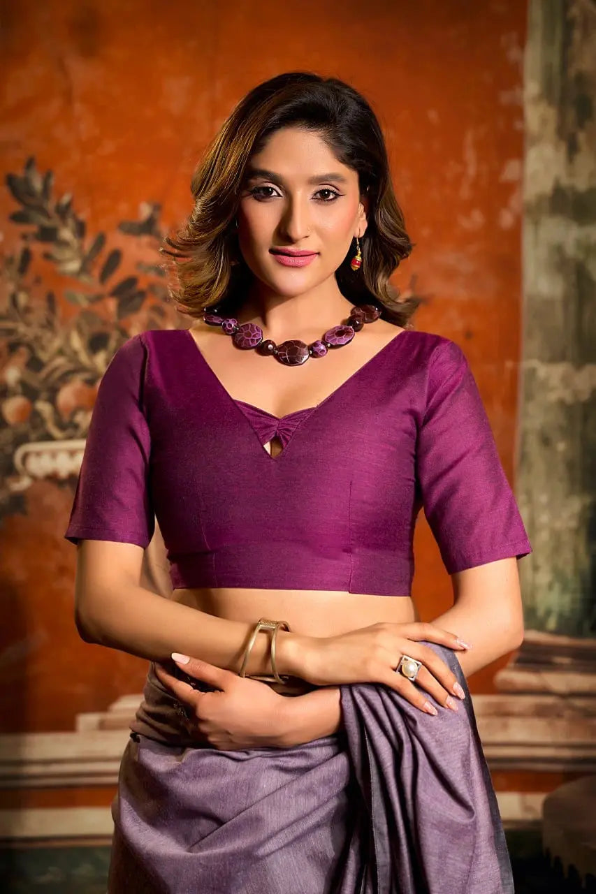 Woman wearing a purple blouse and saree with a textured wall background