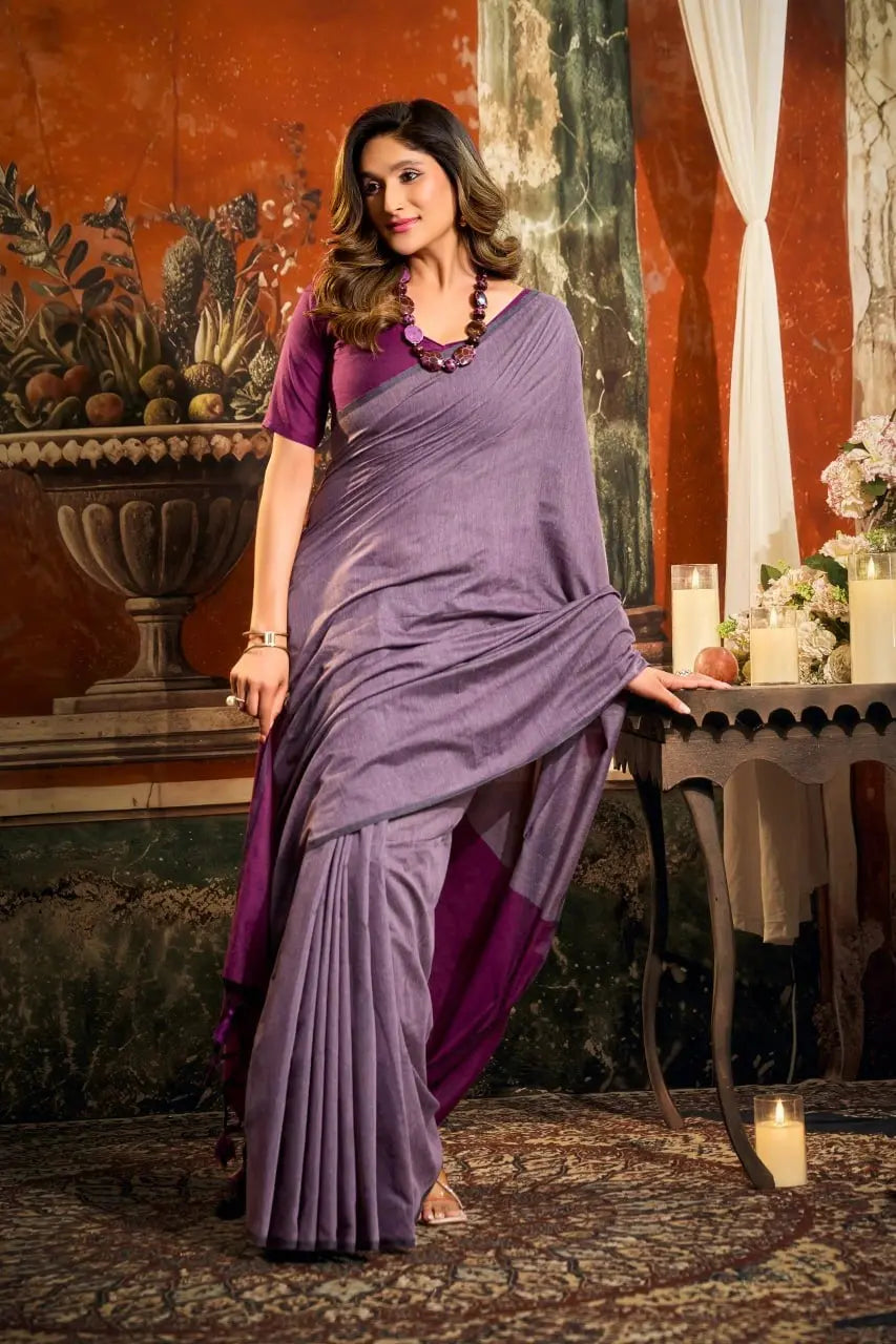 Woman in a purple saree standing in an elegant interior setting.