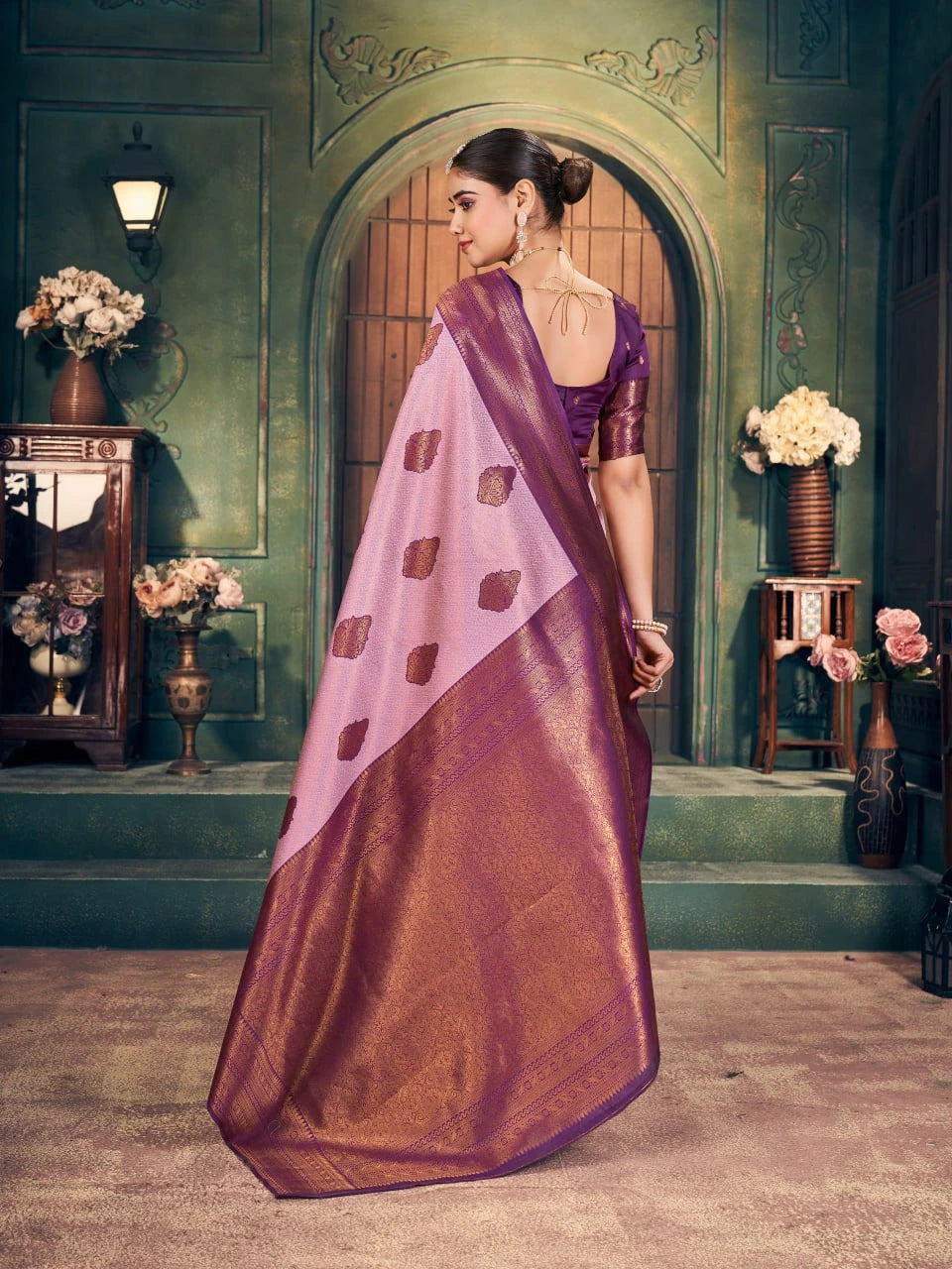 Woman in a traditional saree with a purple blouse and brown saree in an elegant setting.