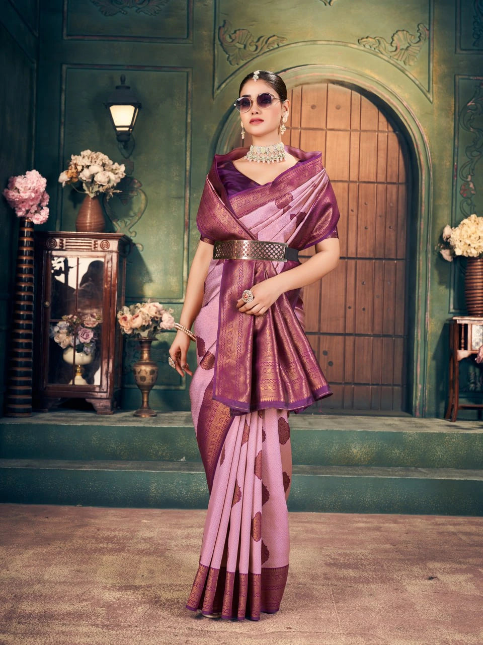 Woman in a traditional pink and purple saree standing in an elegant interior setting.