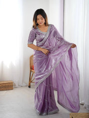 Woman wearing a purple saree with silver border in a minimal indoor setting