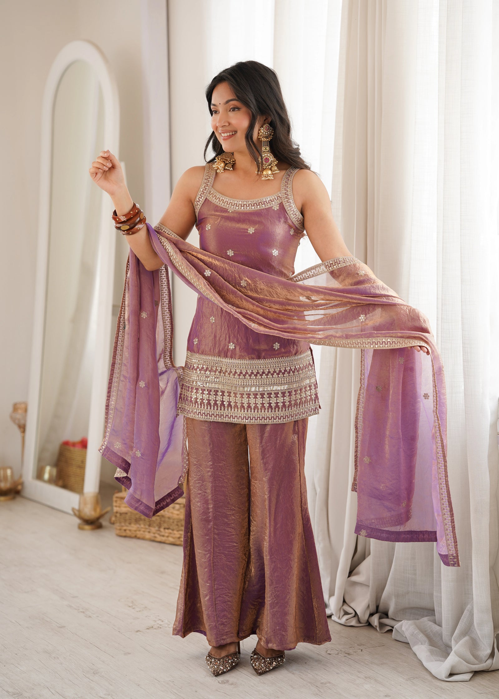 Woman in a traditional outfit with a purple dupatta in a well-lit room.