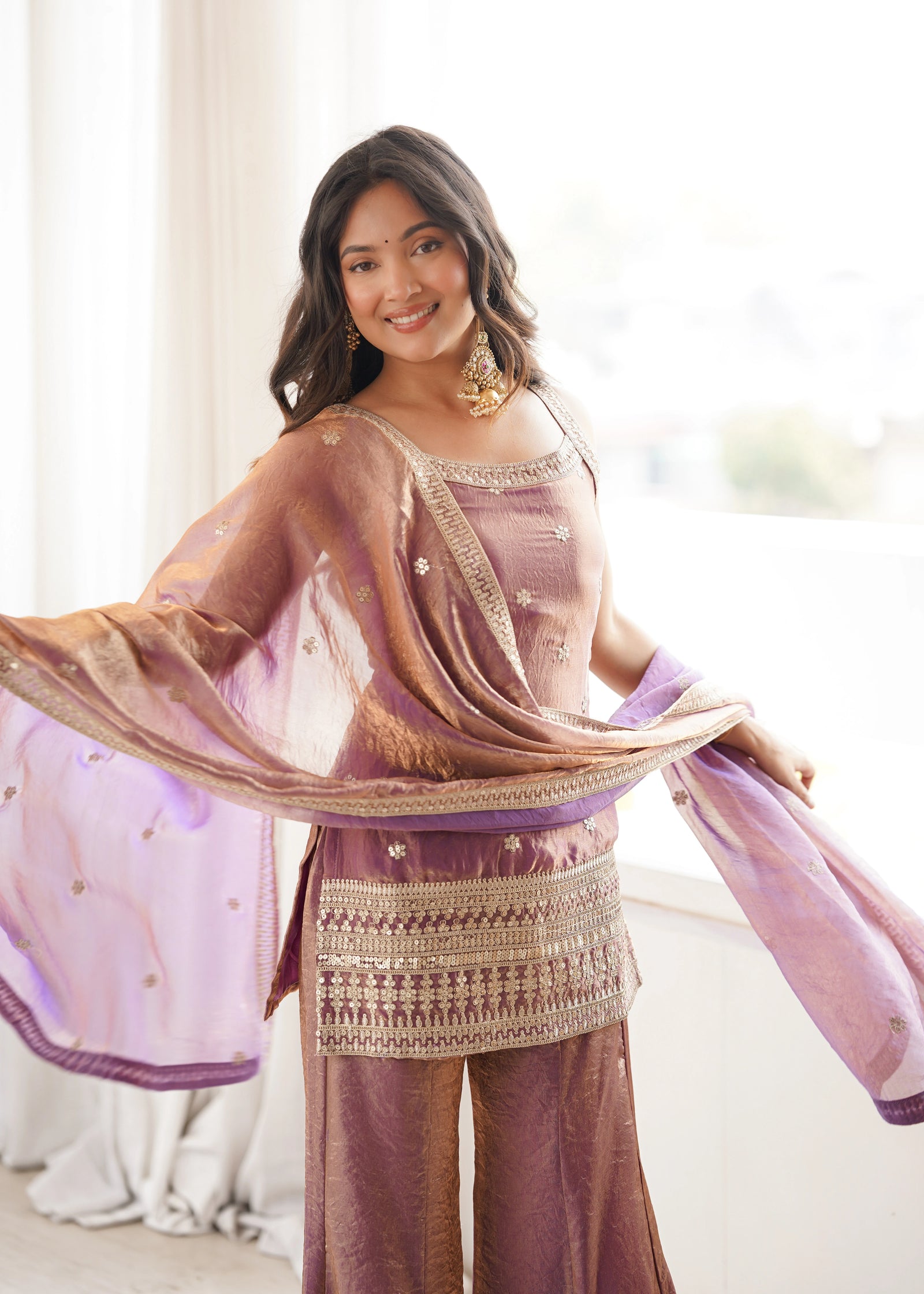 Woman wearing a traditional outfit with a pink dupatta in a bright room.