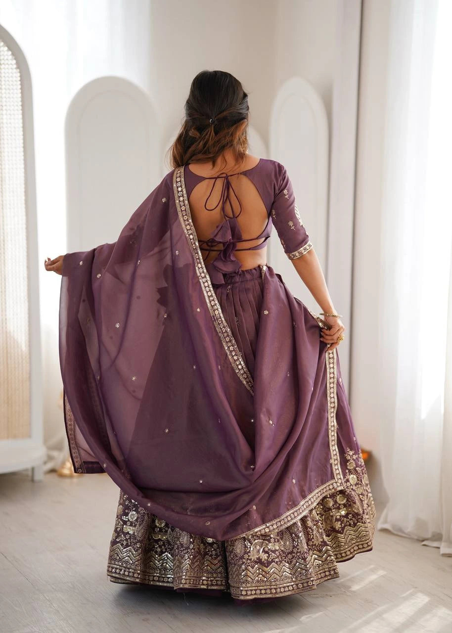 Woman wearing a purple traditional outfit with intricate designs, standing in a bright room.