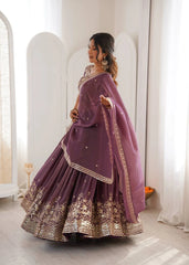 Woman in a purple traditional outfit with gold embroidery standing in a bright room.