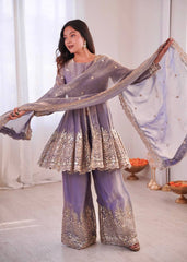 Woman in a lavender traditional outfit with gold embroidery, holding a dupatta.