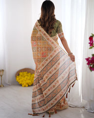 Woman wearing a patterned saree in a bright room with white curtains and flowers.