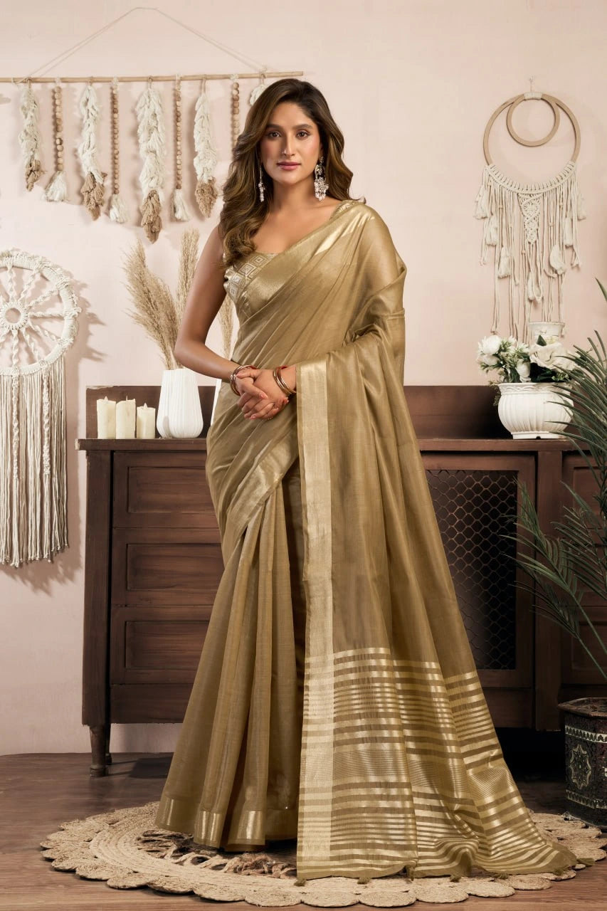 Woman in a gold saree standing in a decorated room with wooden furniture and decorative items.