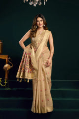 Woman in a beige saree with floral patterns on a dark background