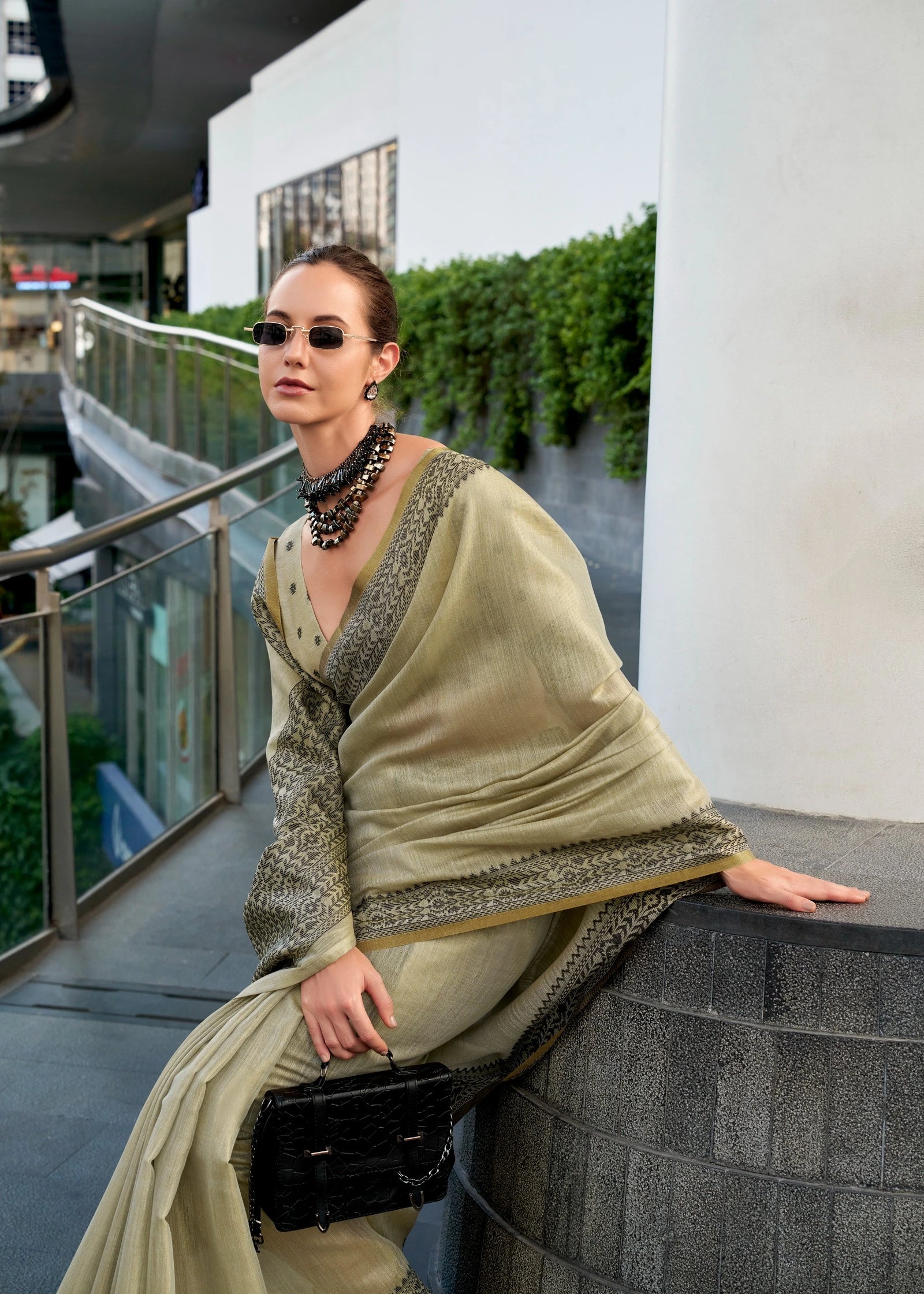 Woman in a light green traditional outfit with sunglasses and a black handbag on a balcony.