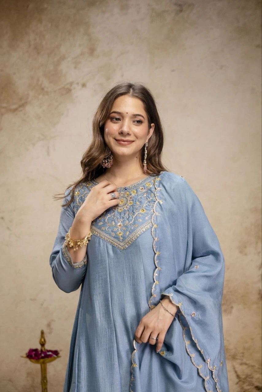 Woman wearing a light blue embroidered traditional outfit against a beige background