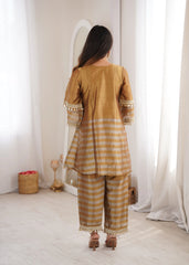 Woman wearing a mustard yellow traditional outfit with white stripes in a minimalistic room.