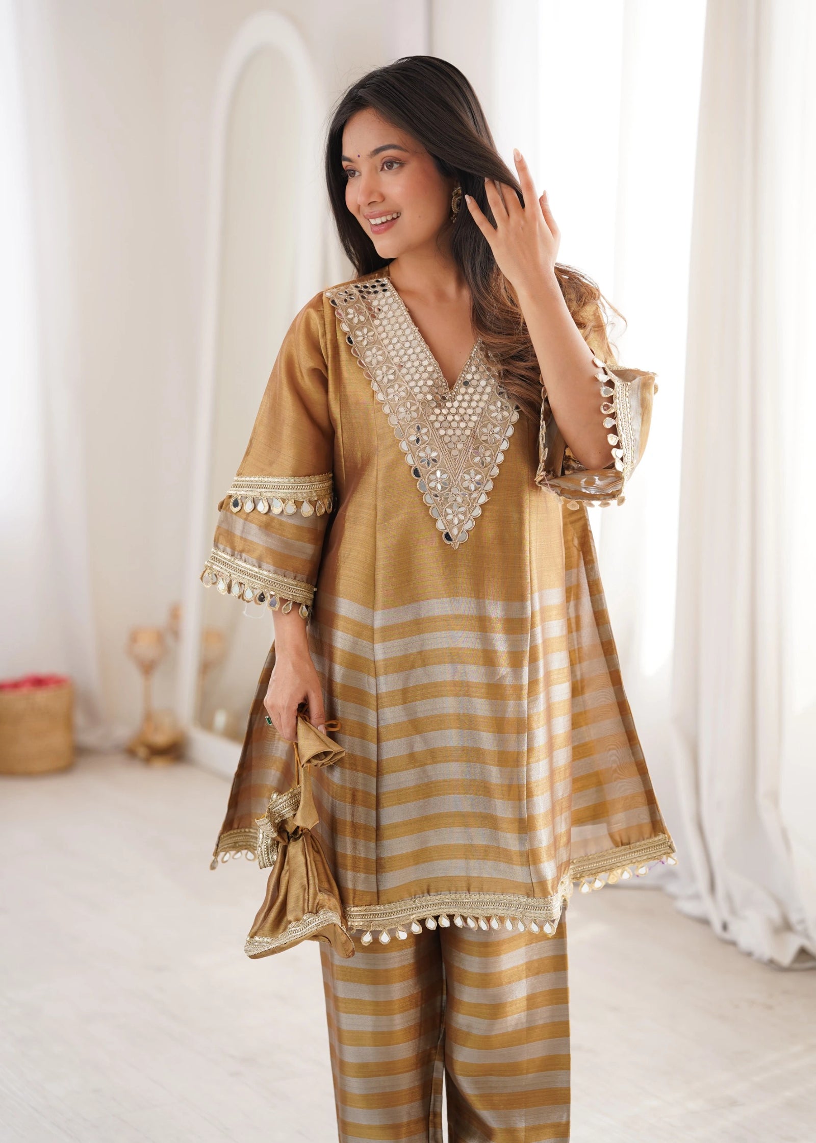 Woman wearing a mustard yellow and white striped outfit with decorative elements, standing in a softly lit room.