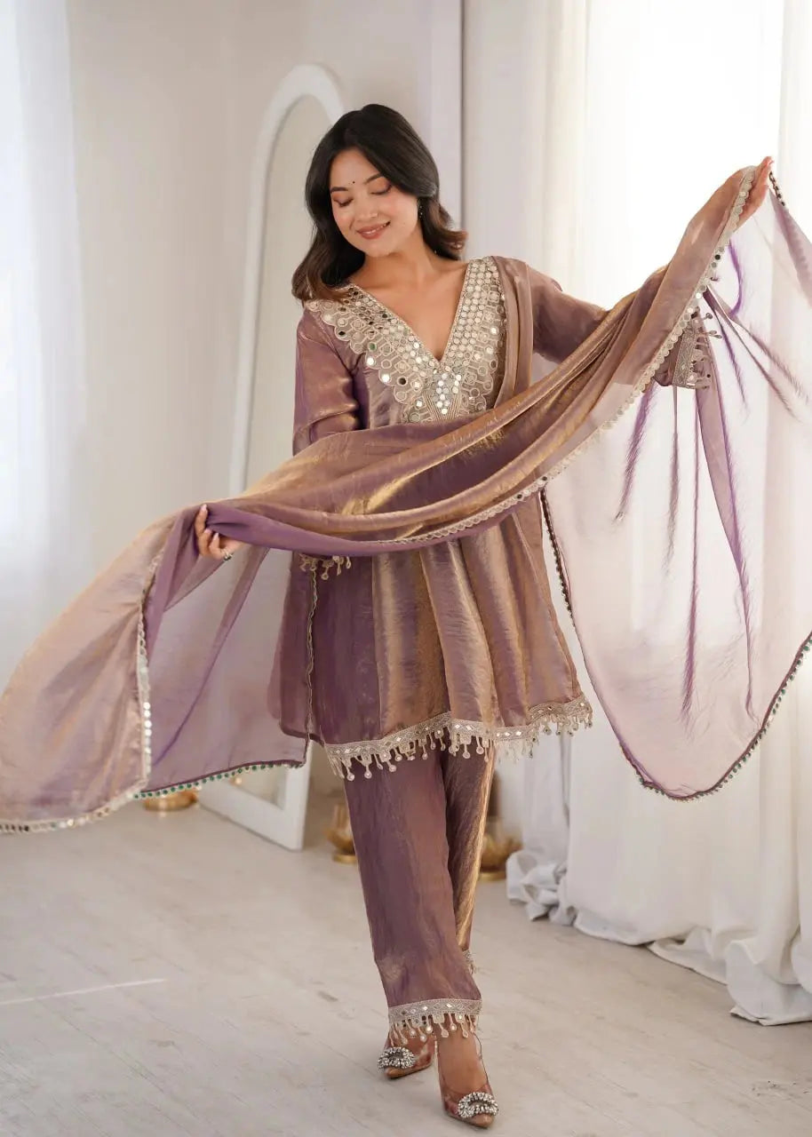Woman in a traditional outfit with a sheer dupatta, standing indoors.