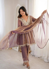 Woman in a traditional outfit with a sheer dupatta, standing indoors.