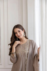 Woman wearing a beige embroidered dress against a neutral background
