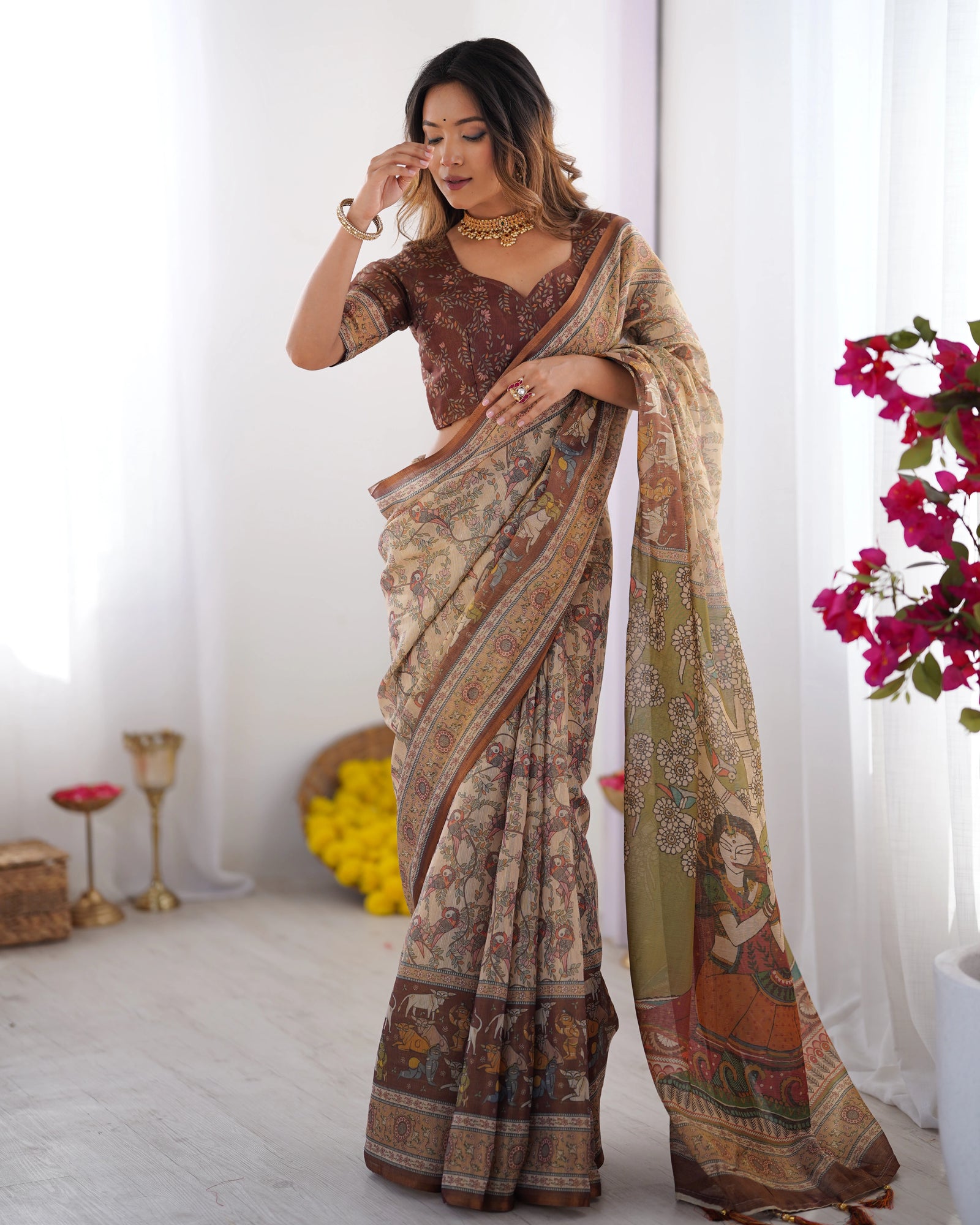 Woman wearing a patterned saree in a bright room with flowers and candles.