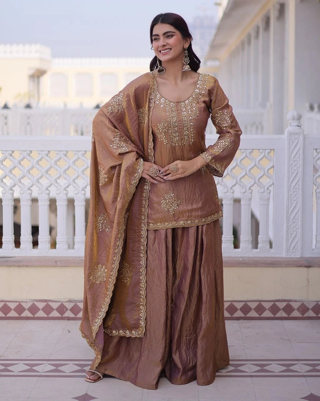 Woman in a traditional brown outfit with gold embroidery standing on a balcony.