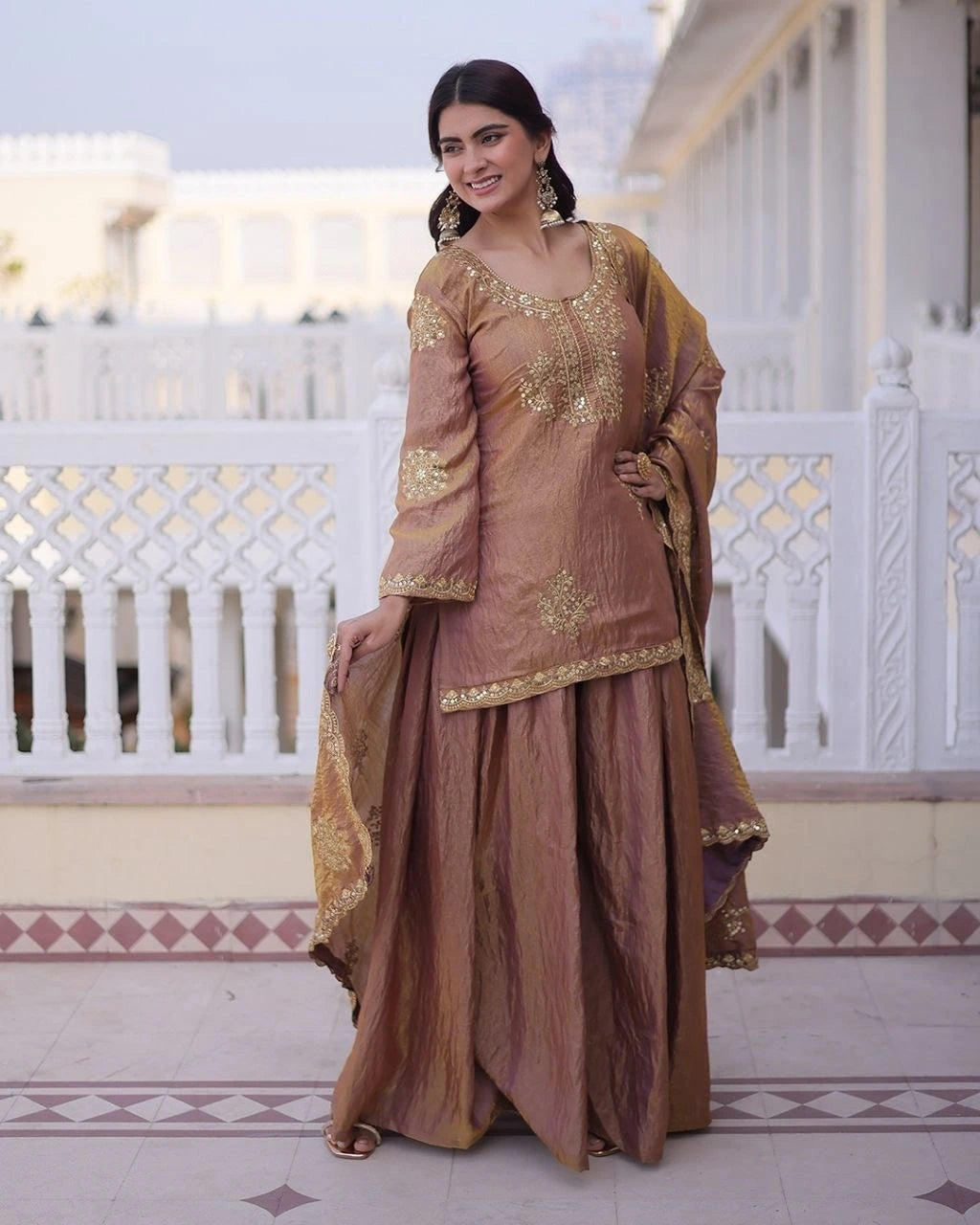 Woman in traditional brown and gold outfit standing on a balcony.