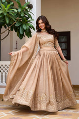 Woman in a beige embroidered traditional outfit standing indoors with decorative elements.