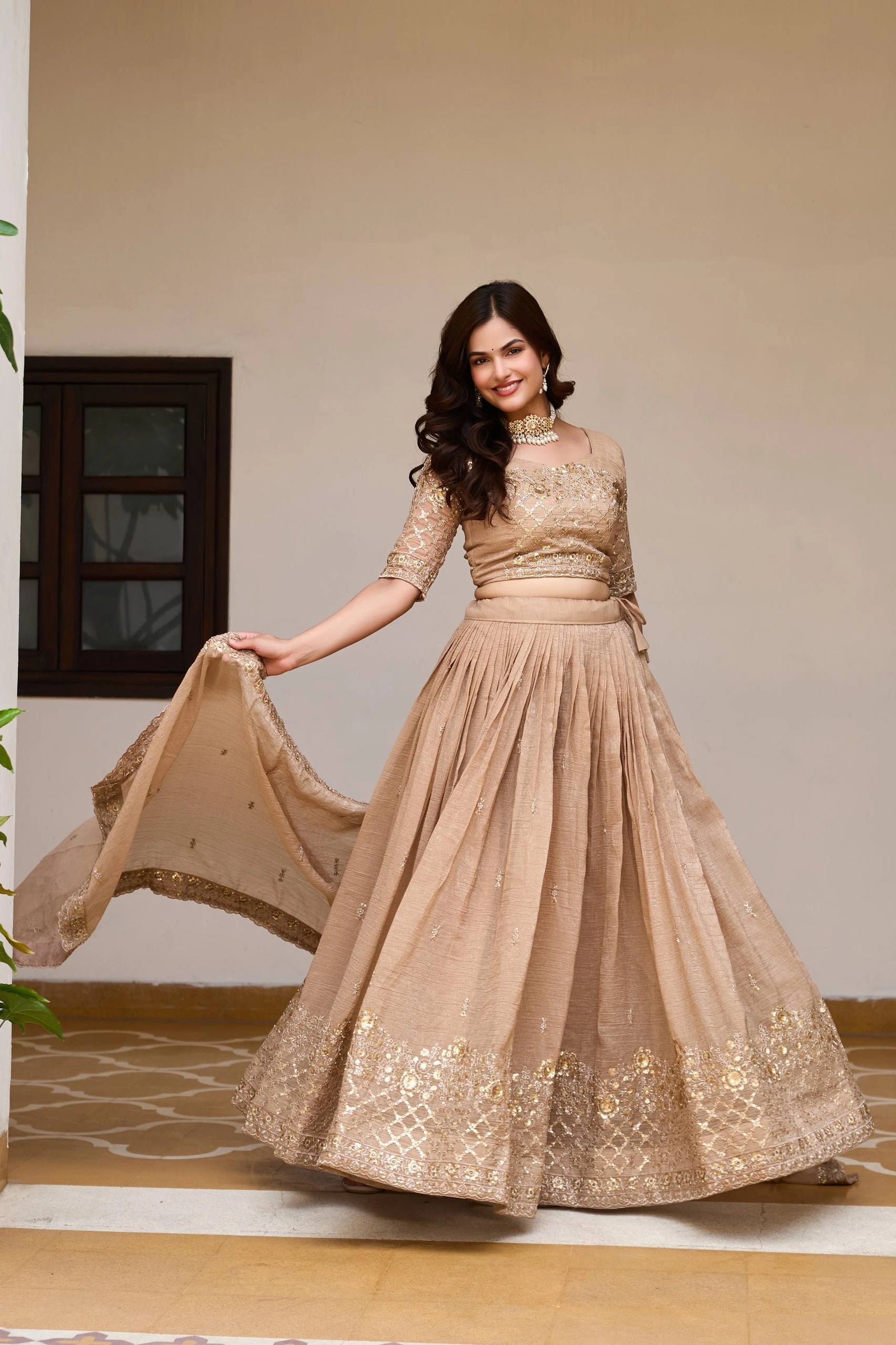 Woman in a beige embroidered gown holding a dupatta indoors.