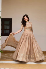 Woman in a beige embroidered gown holding a dupatta indoors.